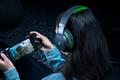 Someone with a black and green over-ear headset on playing a racing game on their phone using a controller.
